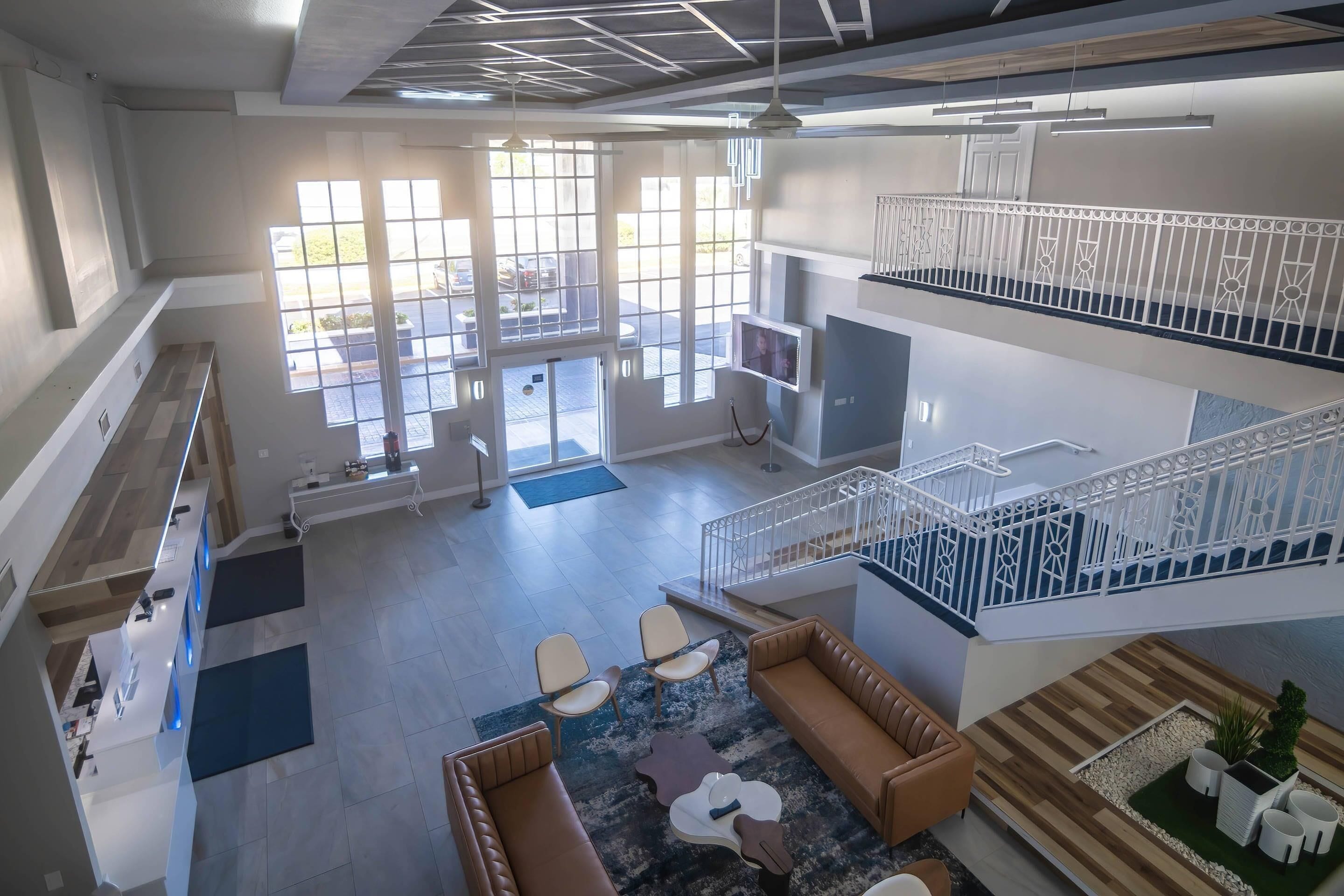 A spacious interior with a reception desk, seating area, staircase, and large windows.