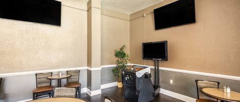A room with a flat-screen TV mounted on the wall, a jukebox, and several tables and chairs.