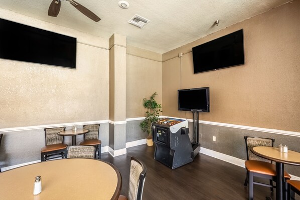 A room with a flat-screen TV mounted on the wall, a jukebox, and several tables and chairs. - Clarion Inn & Suites Central Clearwater Beach (Clearwater)