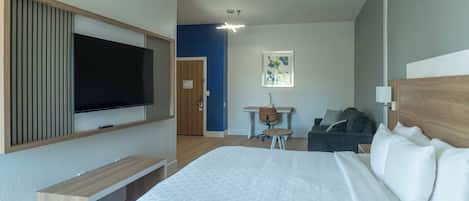 Una habitación de hotel moderna con una cama grande, un televisor montado en la pared, un escritorio con una silla y una mesita con otra silla.