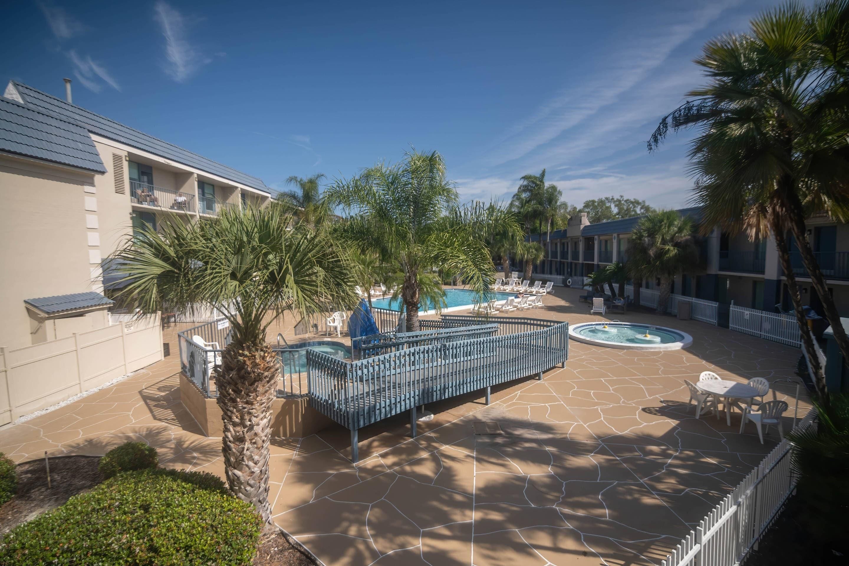 Un patio de hotel con piscina, palmeras y mobiliario exterior.
