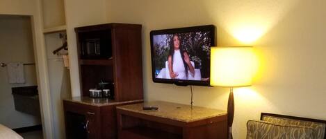 A hotel room with a bed, a desk with a television, a chair, and a lamp.