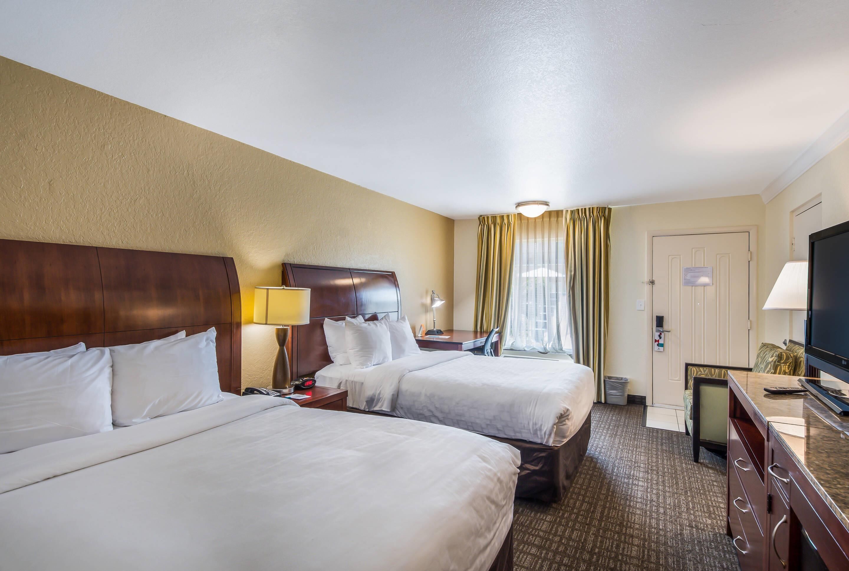 Ein Hotelzimmer mit zwei Betten, einem Fernseher, einem Schreibtisch mit Lampe und einer Tür.