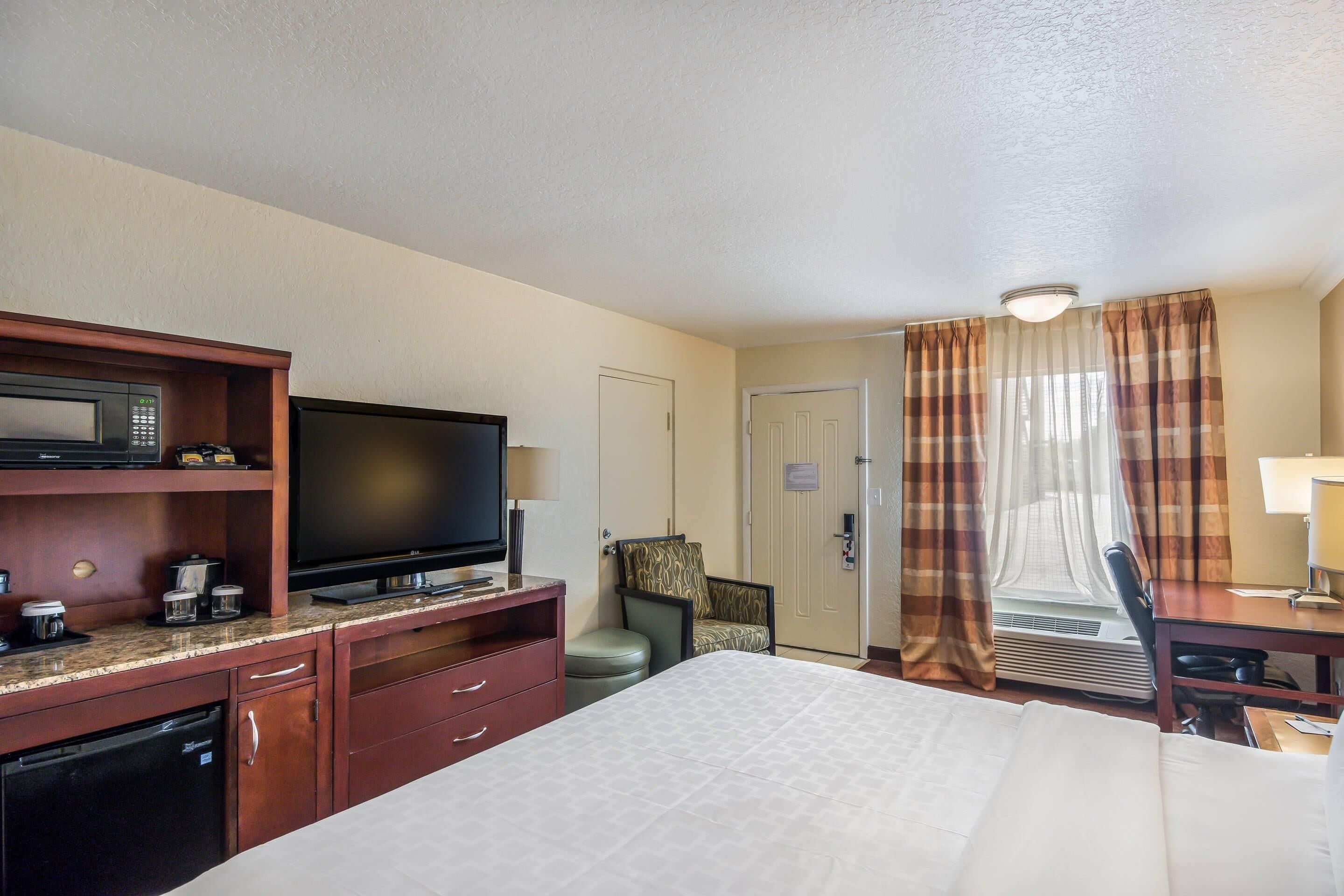 A hotel room with a bed, a television, a desk, a chair, a microwave, and a small refrigerator.
