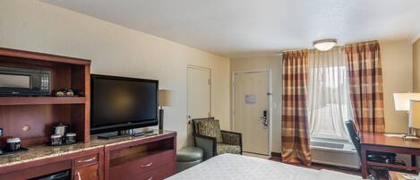 A hotel room with a bed, a television, a desk, a chair, a microwave, and a small refrigerator.