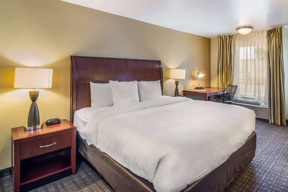 A hotel room with a large bed, two bedside tables, a chair, a desk, and a window with curtains.