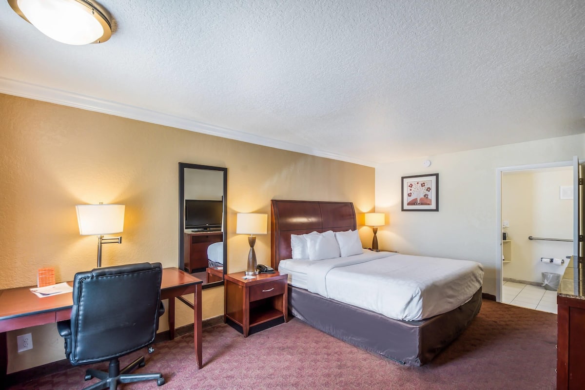 A hotel room with a bed, desk, chair, lamps, and a television.