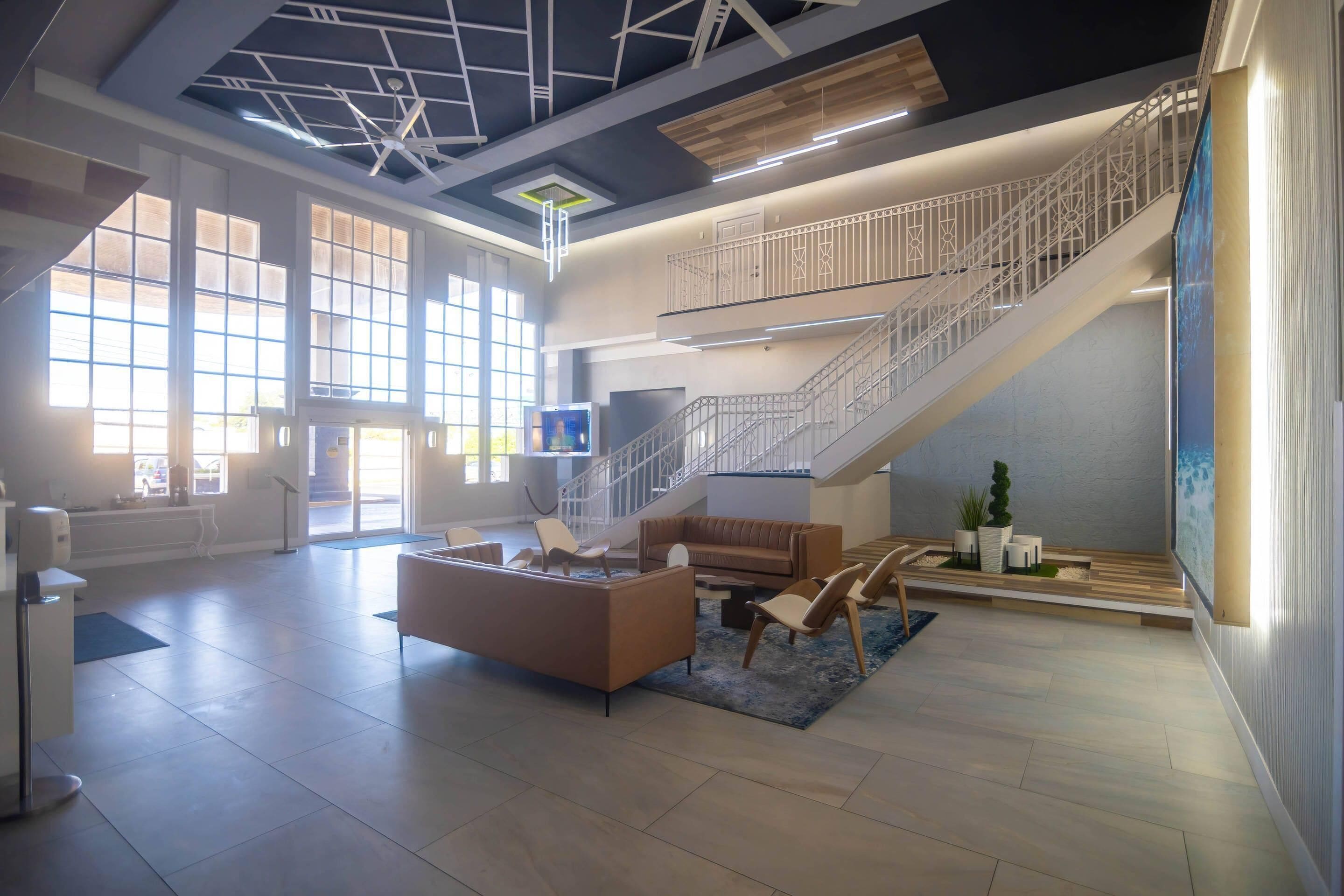 A spacious lobby with a staircase, seating area, and large windows.