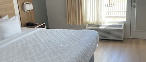 A hotel room with a large bed, a bedside table with a phone, a wall-mounted light, and a window with curtains.