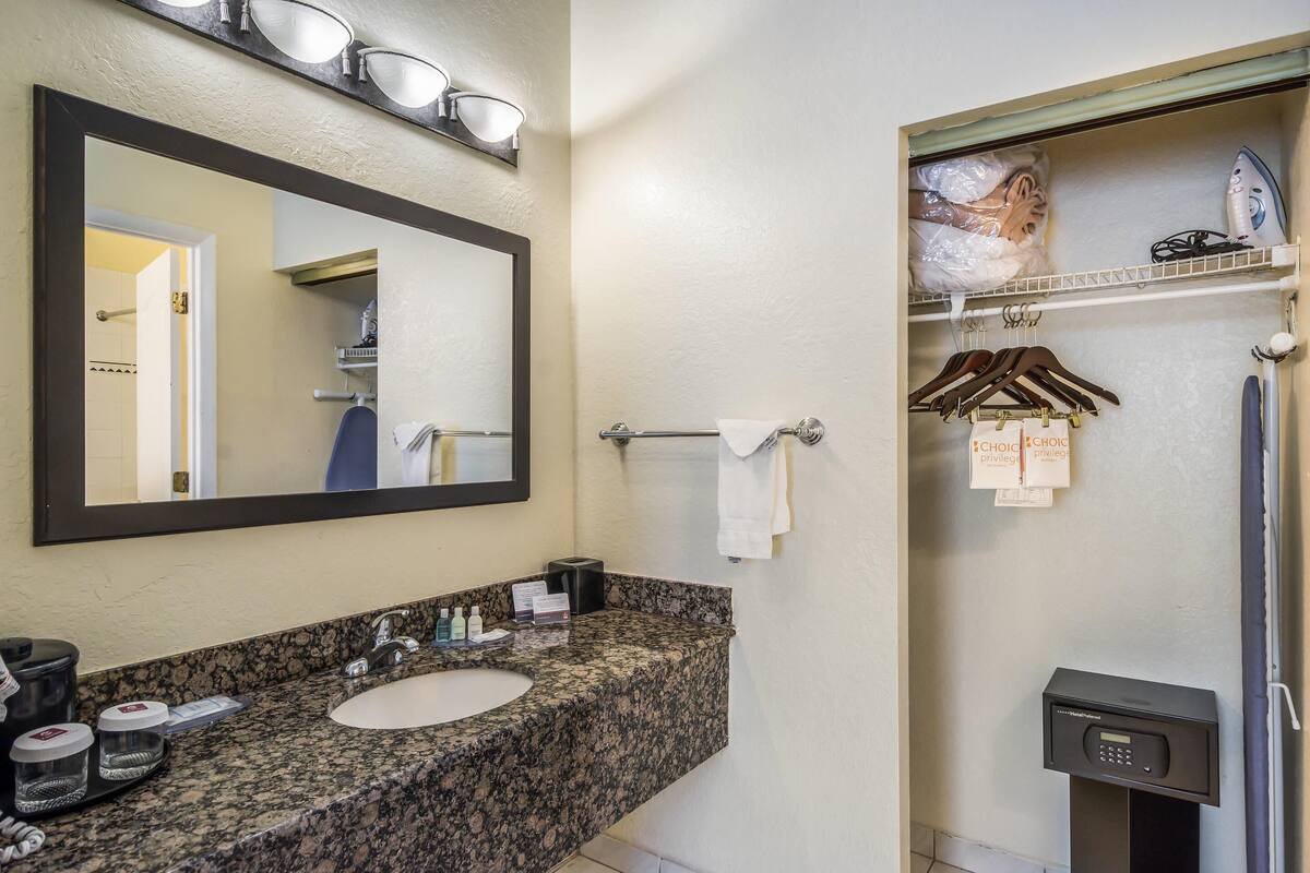A bathroom with a granite countertop sink, a mirror, a towel rack, and a shower area.