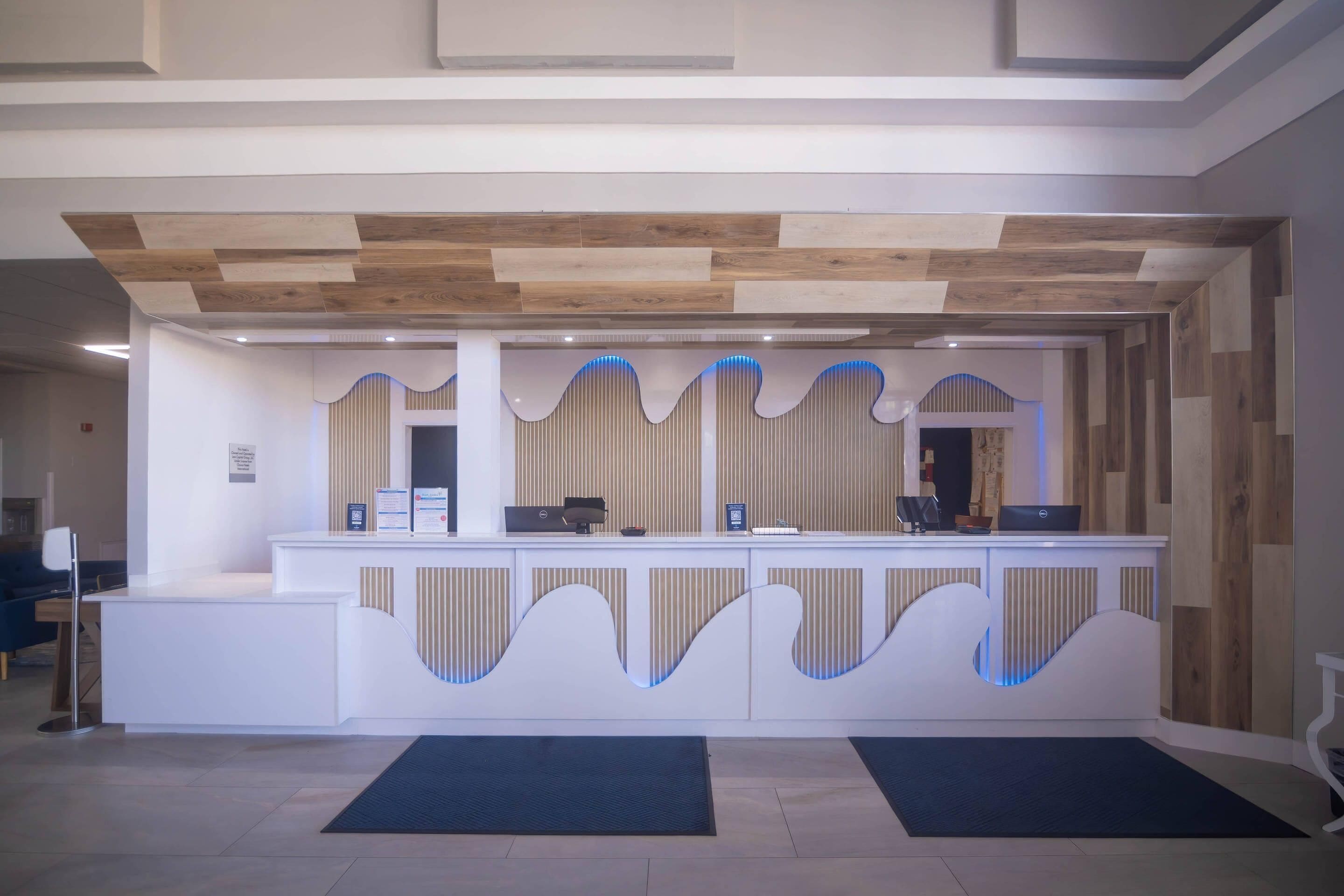 A reception desk with a modern design, a wooden ceiling, and a blue-lit wave pattern on the wall.
