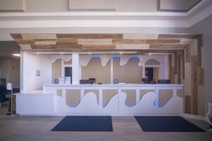 A reception desk with a modern design, a wooden ceiling, and a blue-lit wave pattern on the wall.
