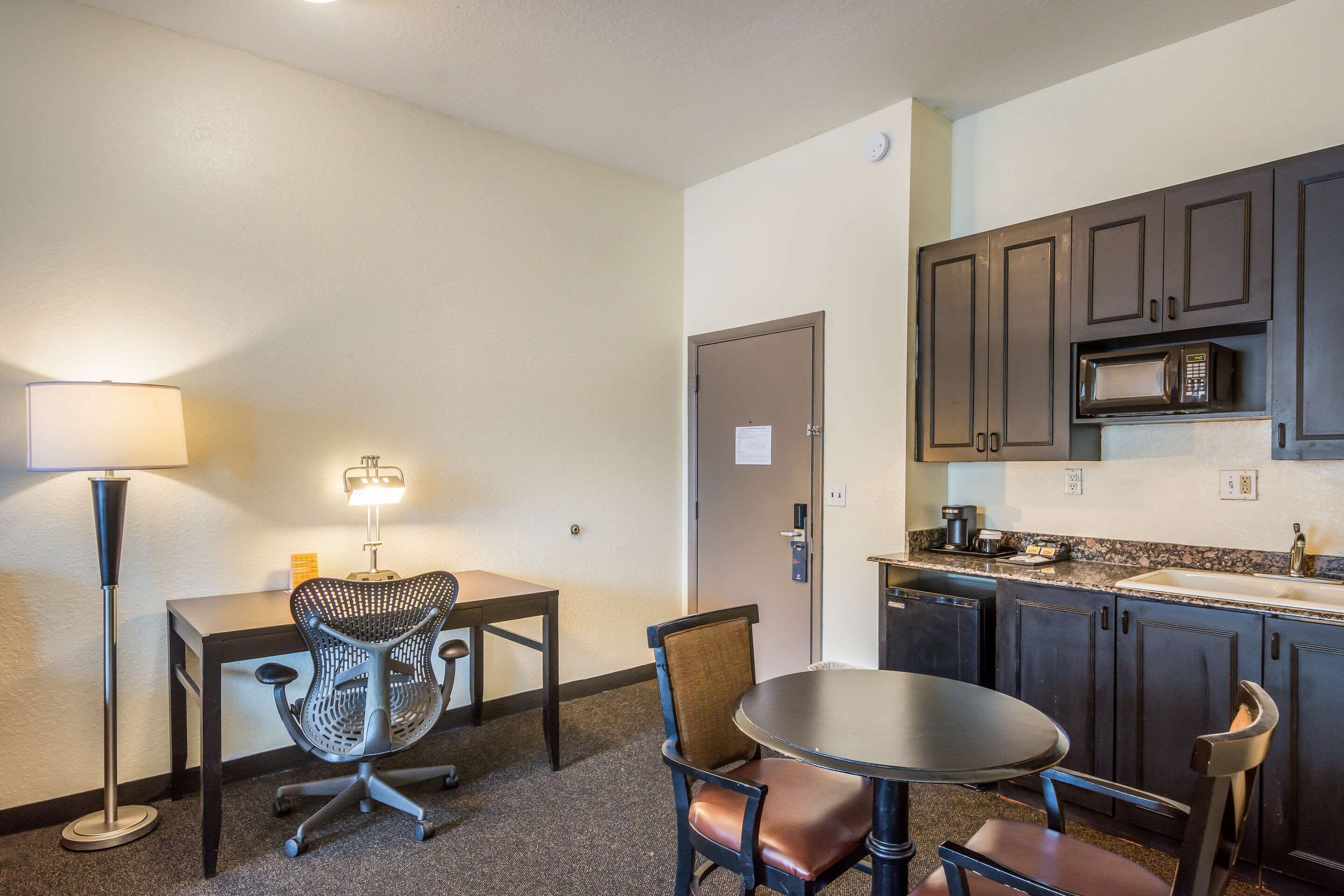 Una habitación de hotel compacta con kitchenette, una zona de comedor con mesa y sillas, y una lámpara.