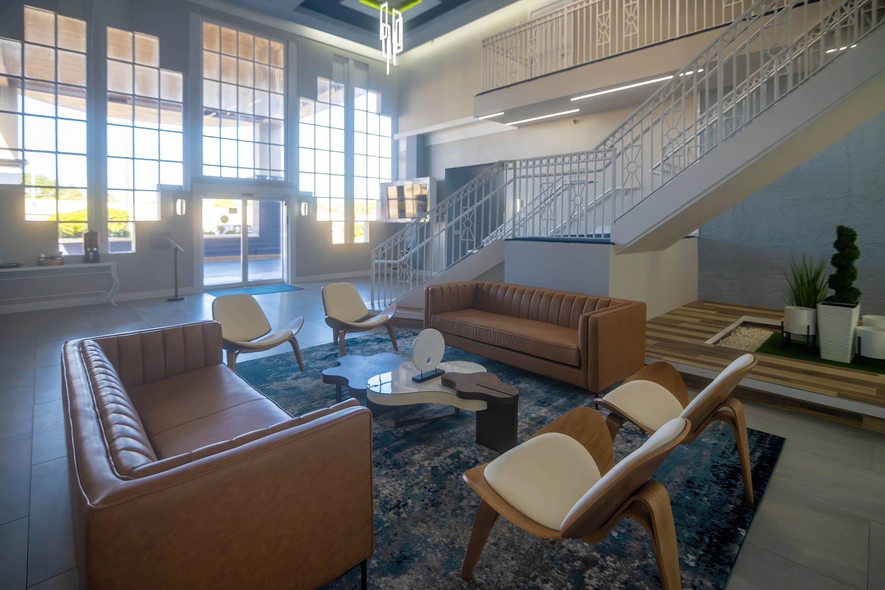 A spacious lobby with a staircase, seating area, and large windows.