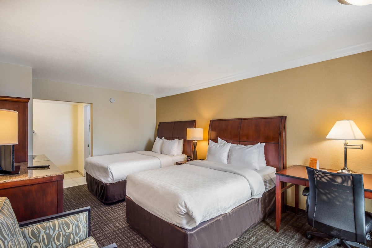 A hotel room with two beds, a desk, a chair, and a television.