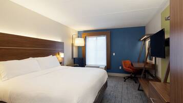 Une chambre d’hôtel avec un grand lit, un bureau avec une chaise, une télévision et une fenêtre avec des stores.