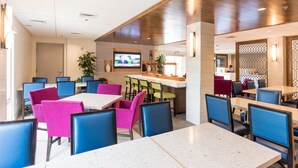 A modern restaurant with a variety of seating options, including tables and booths, and a bar area with a television screen.