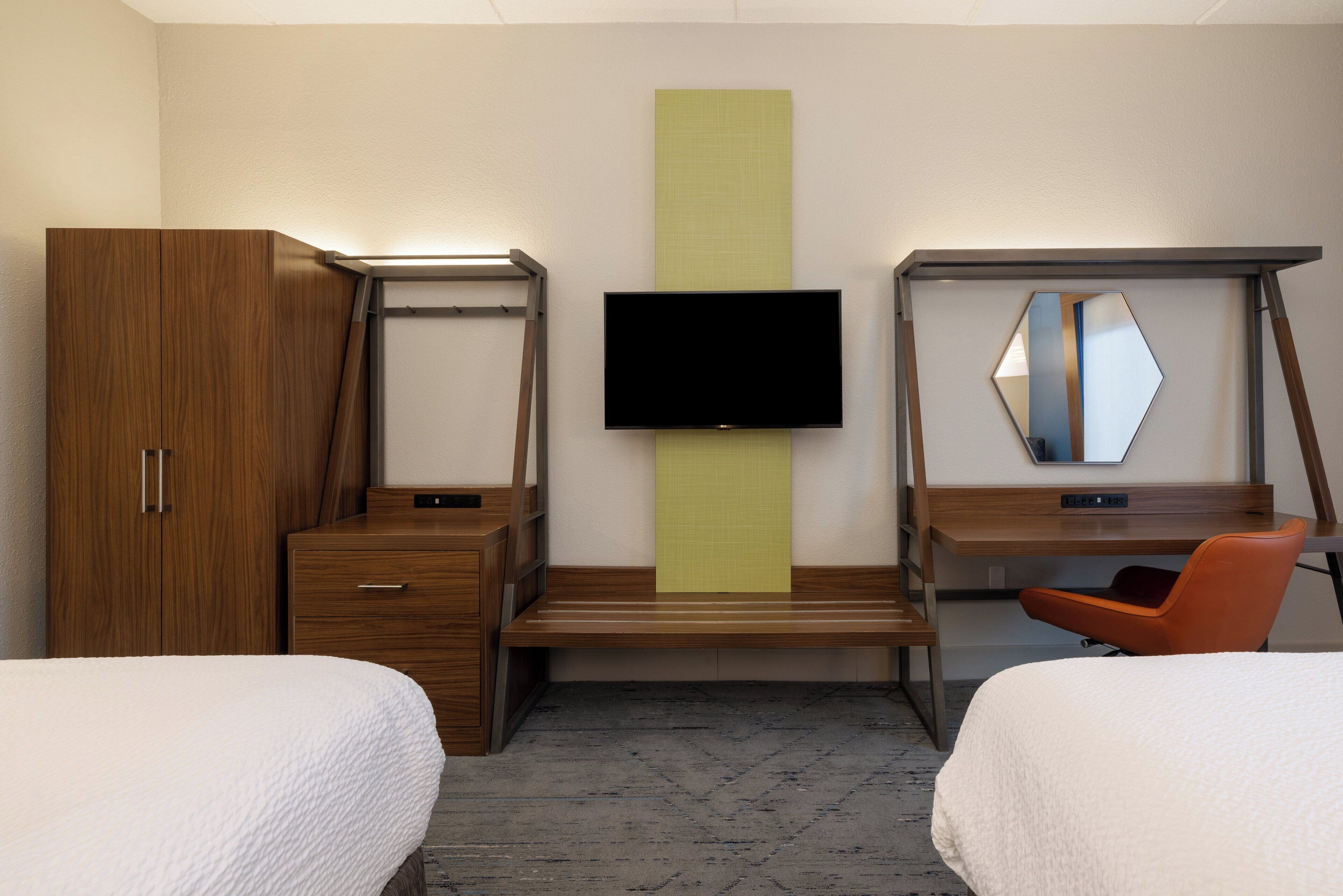 A hotel room with two beds, a desk, a television, and a wardrobe.