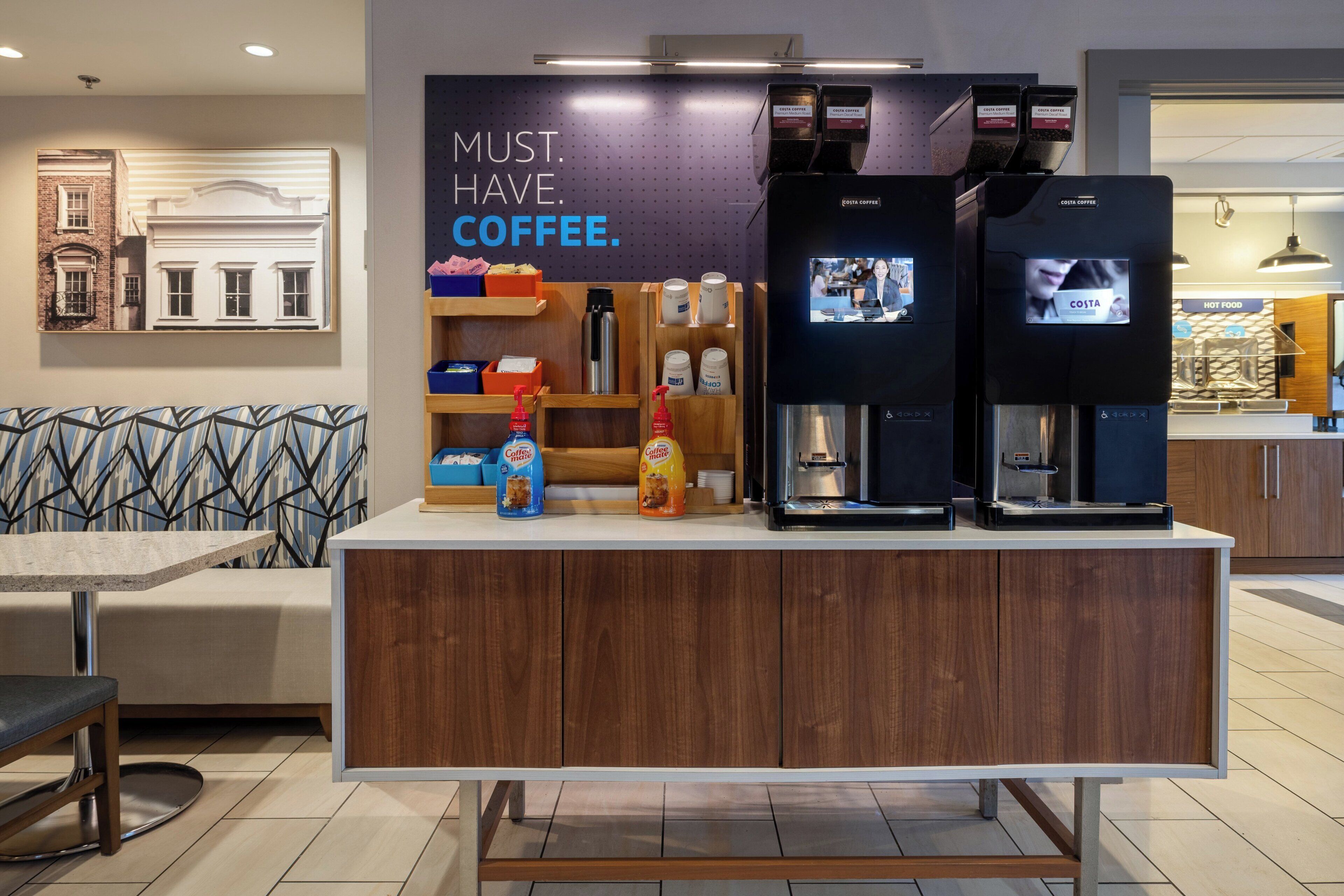 En kaffestation med mærkevarer, et siddeområde med mønstrede hynder og en væg med en kaffebesked.