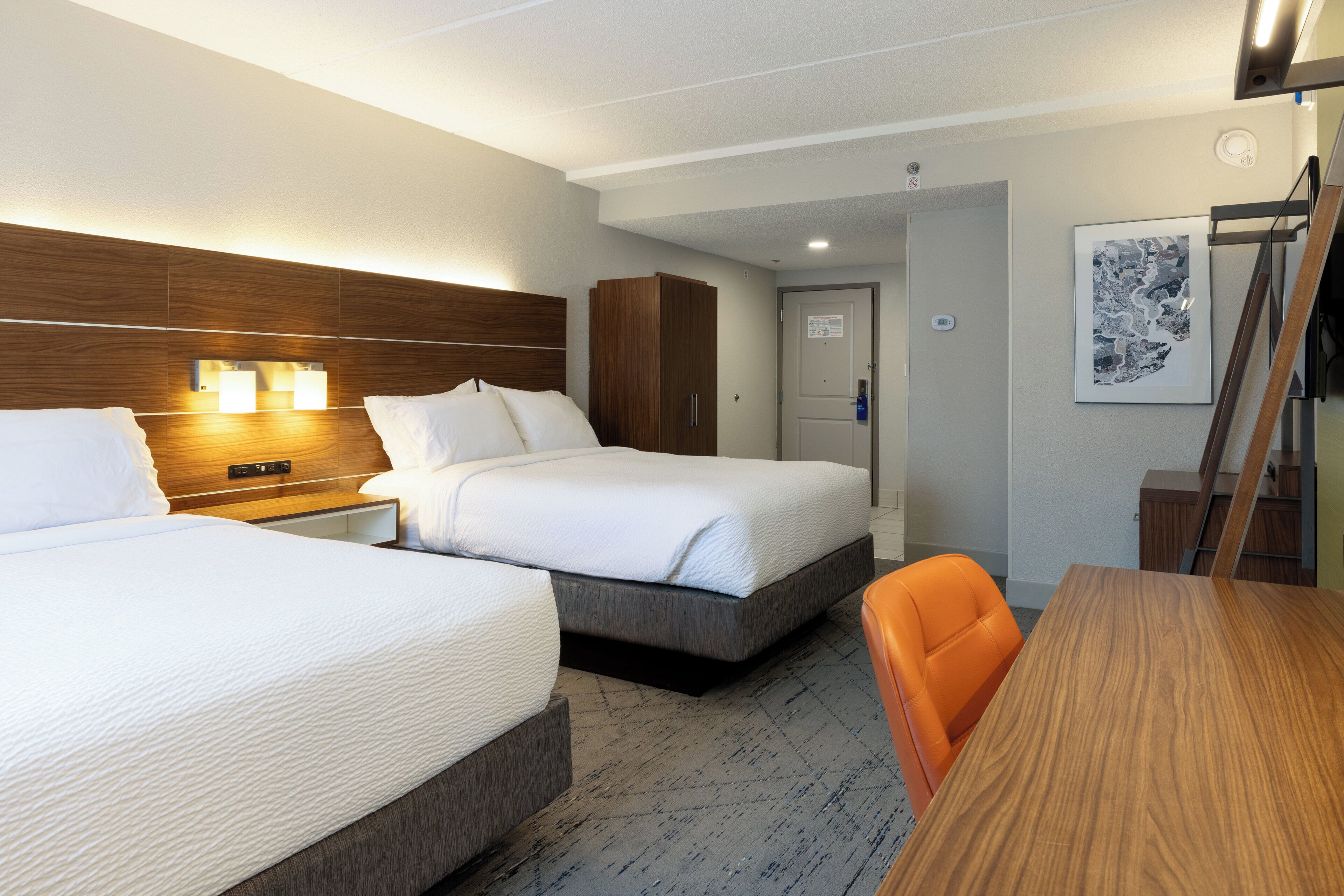 A hotel room with two beds, a wooden headboard, a desk, and an orange chair.