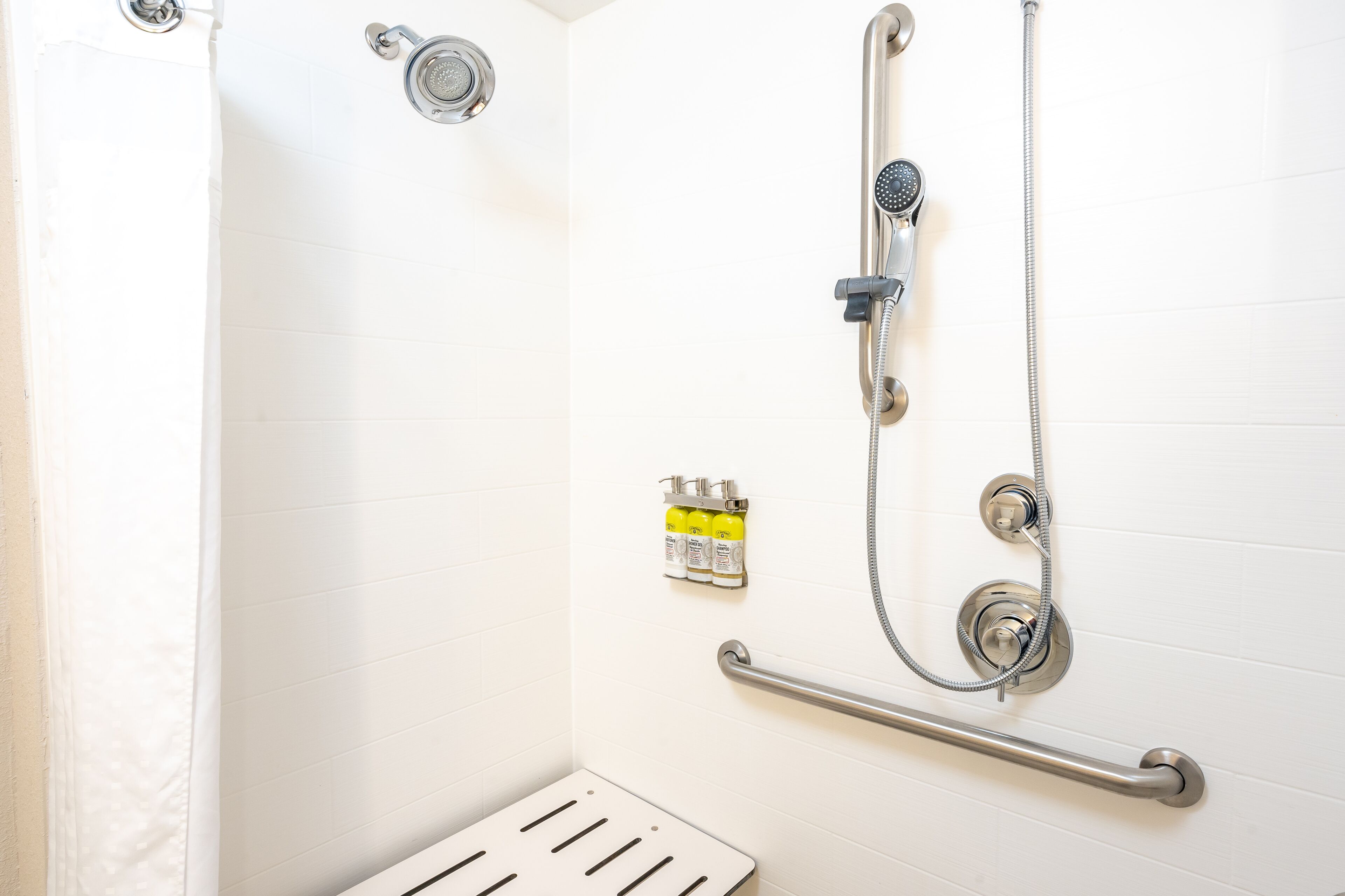 A shower with a handheld showerhead, a wall-mounted faucet, and a handheld shower hose. There is a grab bar installed for safety.