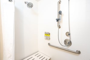 A shower with a handheld showerhead, a wall-mounted faucet, and a handheld shower hose. There is a grab bar installed for safety.