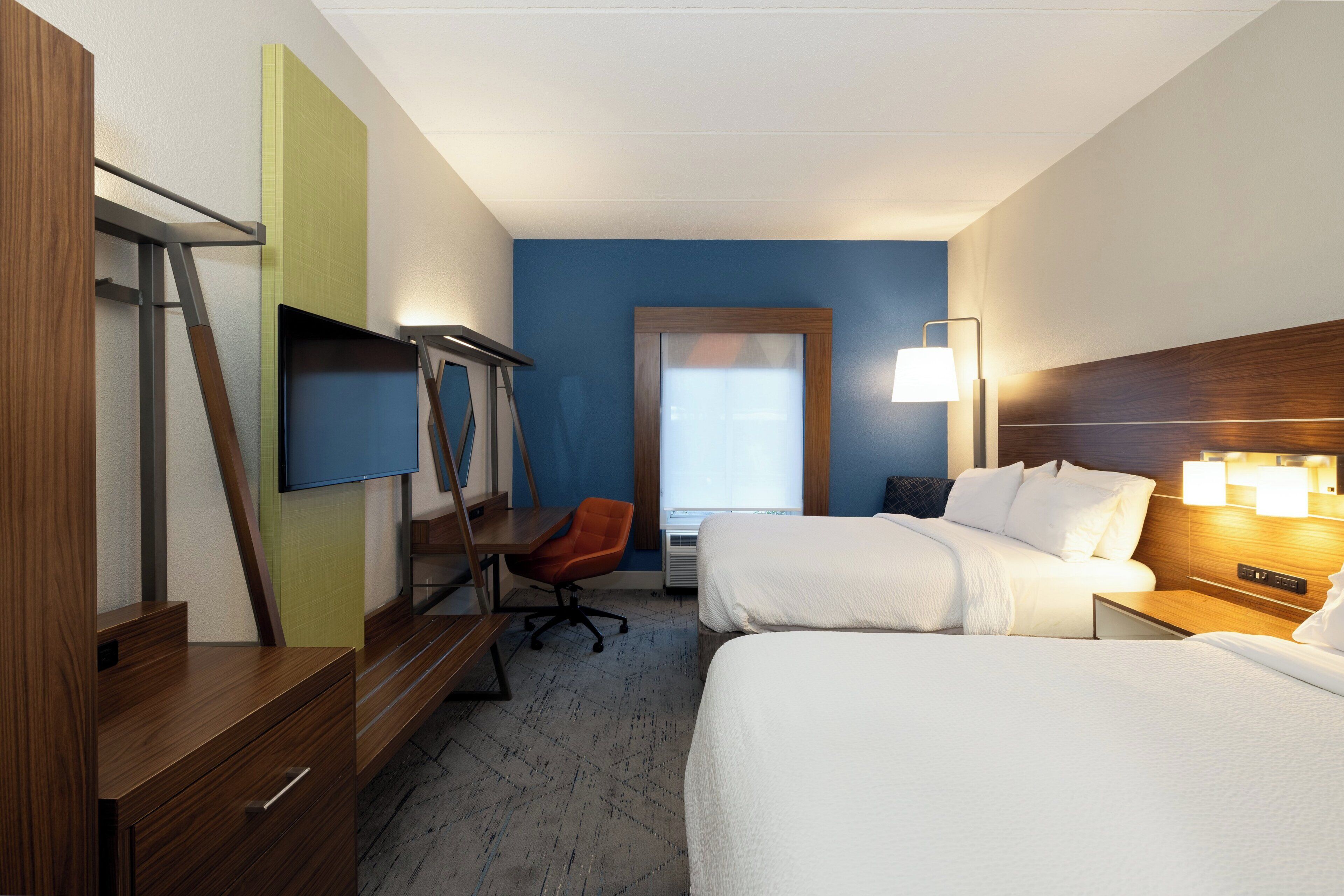 A hotel room with two beds, a desk, a chair, a TV, and a window.