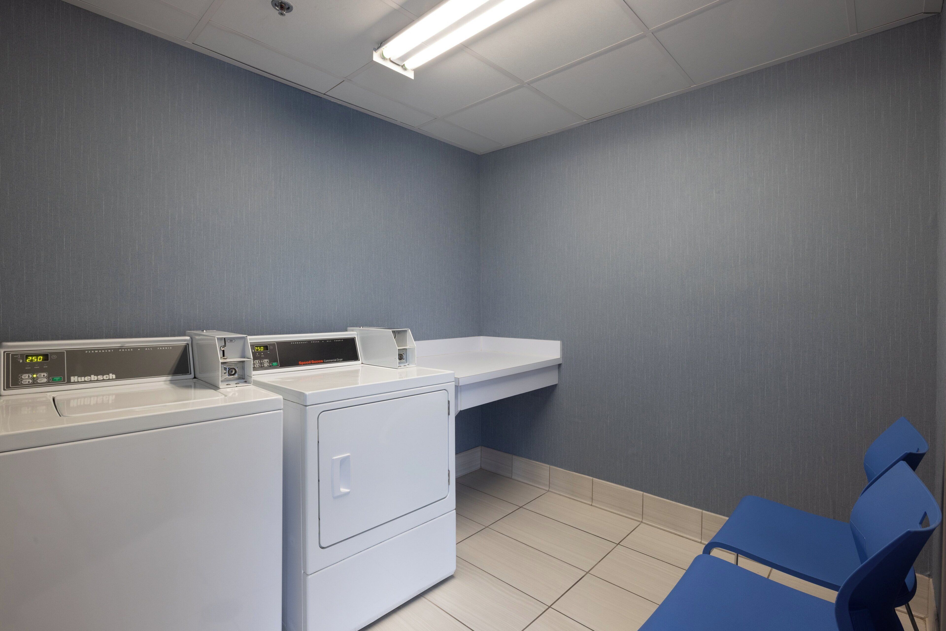 A laundry room with a front-loading washer and dryer, a blue chair, and a shelf above the dryer.