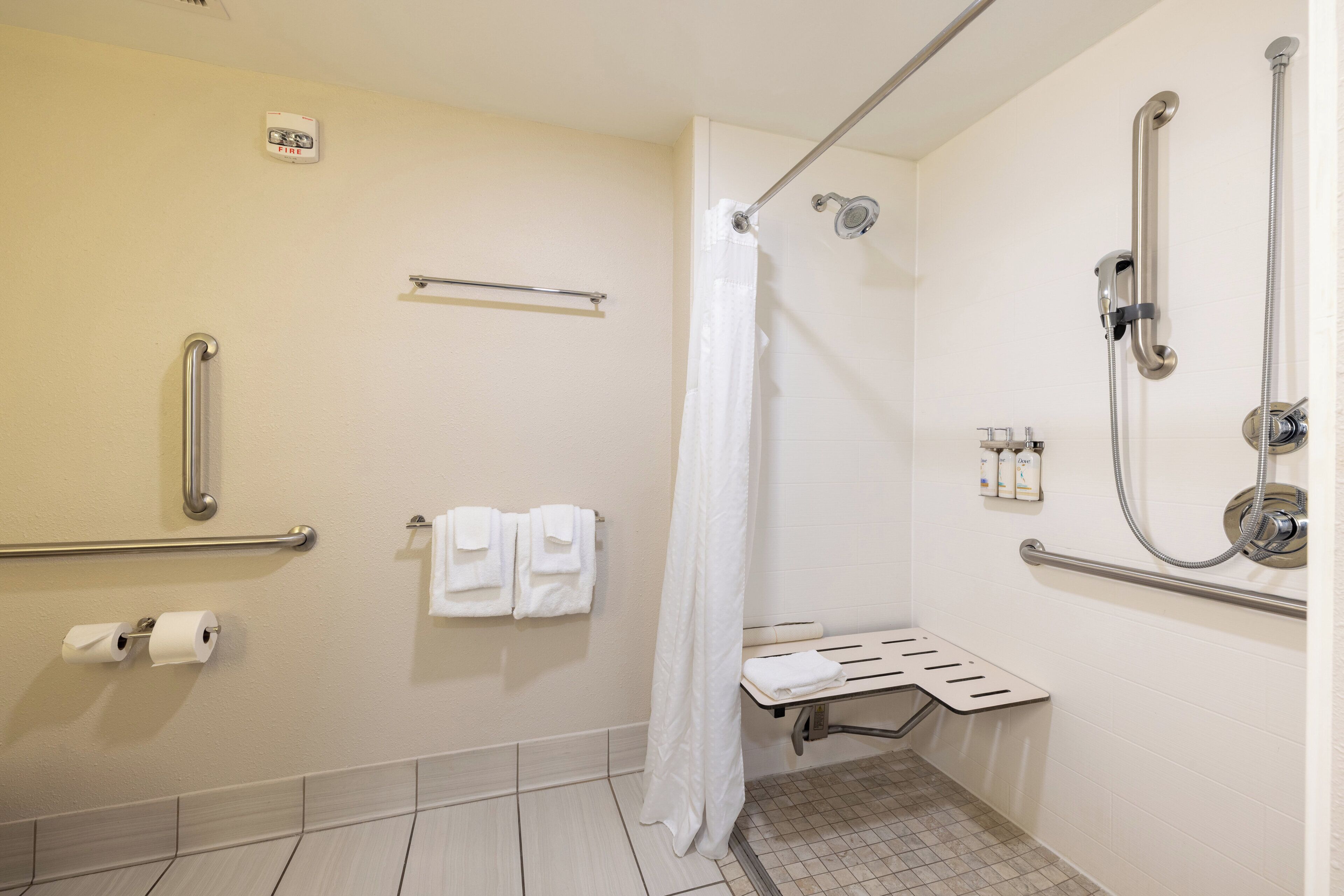 A bathroom with a shower, grab bars, a towel rack, and a toilet paper holder.