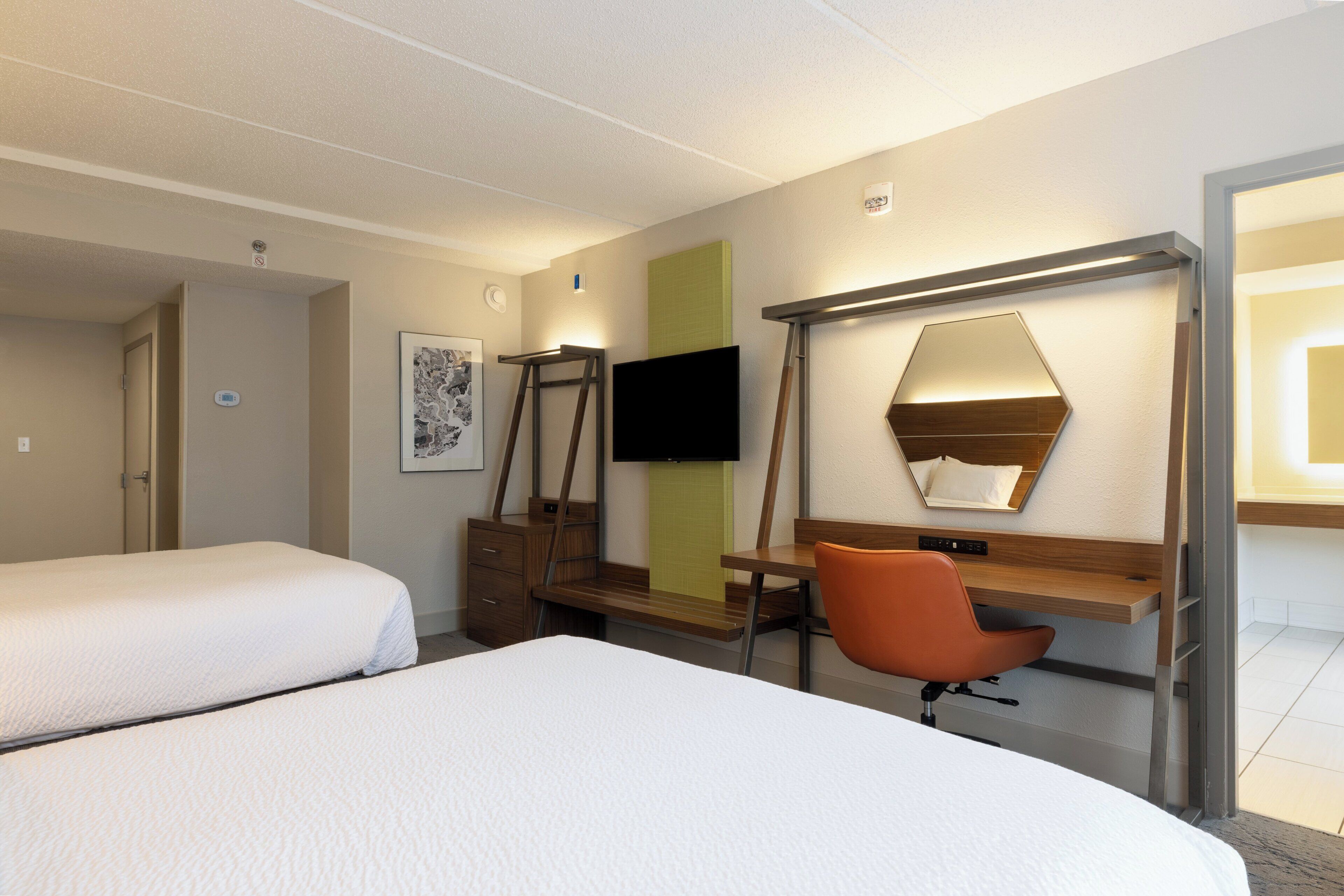 A hotel room with two beds, a desk with a chair, a television, and a mirror.