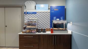 Mostrador de panadería con un letrero que dice '¿QUÉ TAL UN COMIENZO CALIENTE?' y una vitrina con productos horneados.