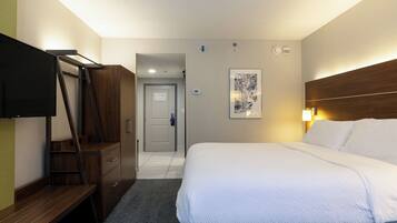 A hotel room with a bed, a desk, a TV, and a door leading to a hallway.