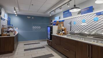 Un área de desayuno moderna con una pared azul, un panel digital de menú y una barra con recipientes etiquetados.
