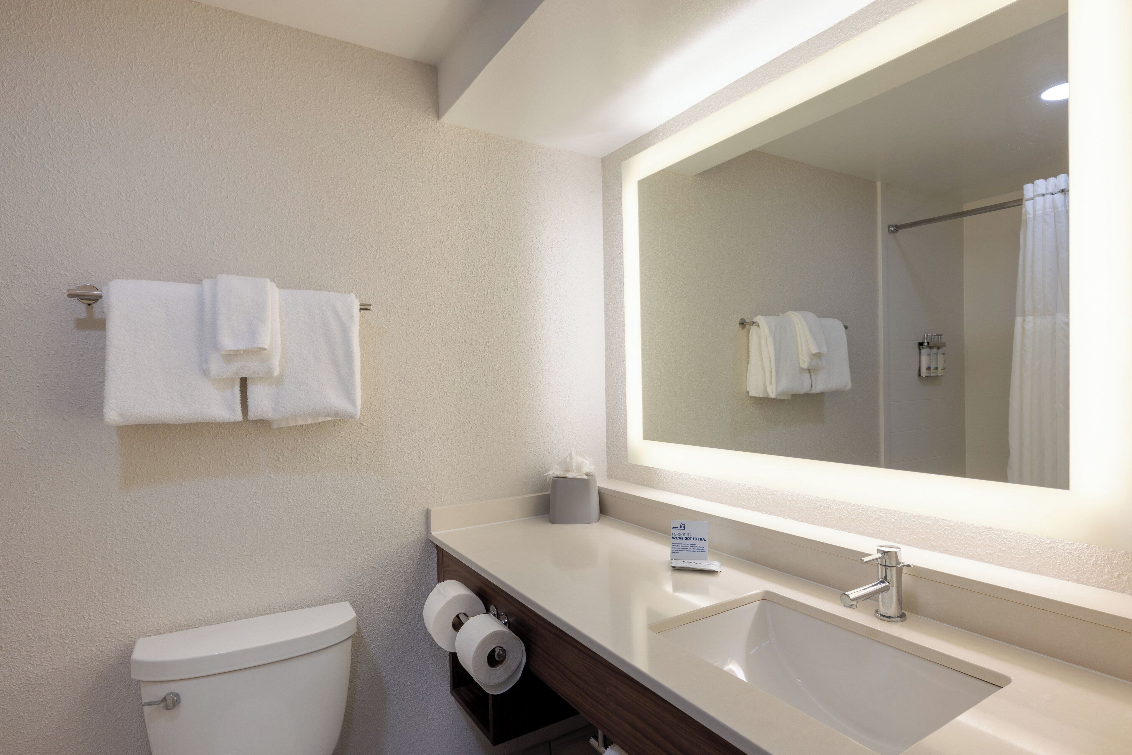 A bathroom with a toilet, sink, mirror, and towels.