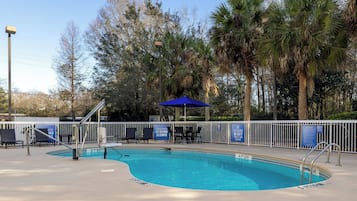 A swimming pool with a blue umbrella, surrounded by palm trees and a white fence.