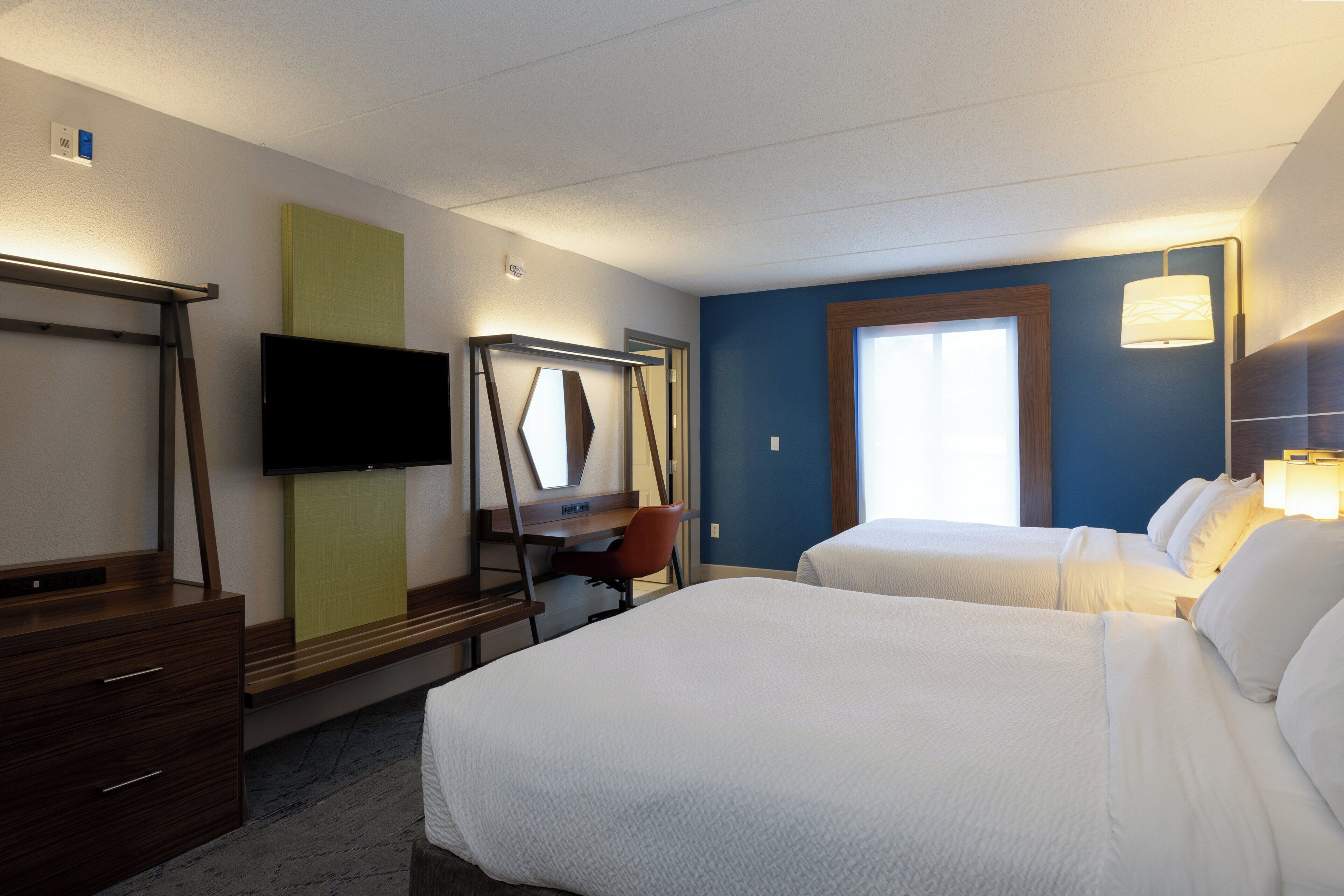 A hotel room with a bed, a desk, a chair, a television, and a window.