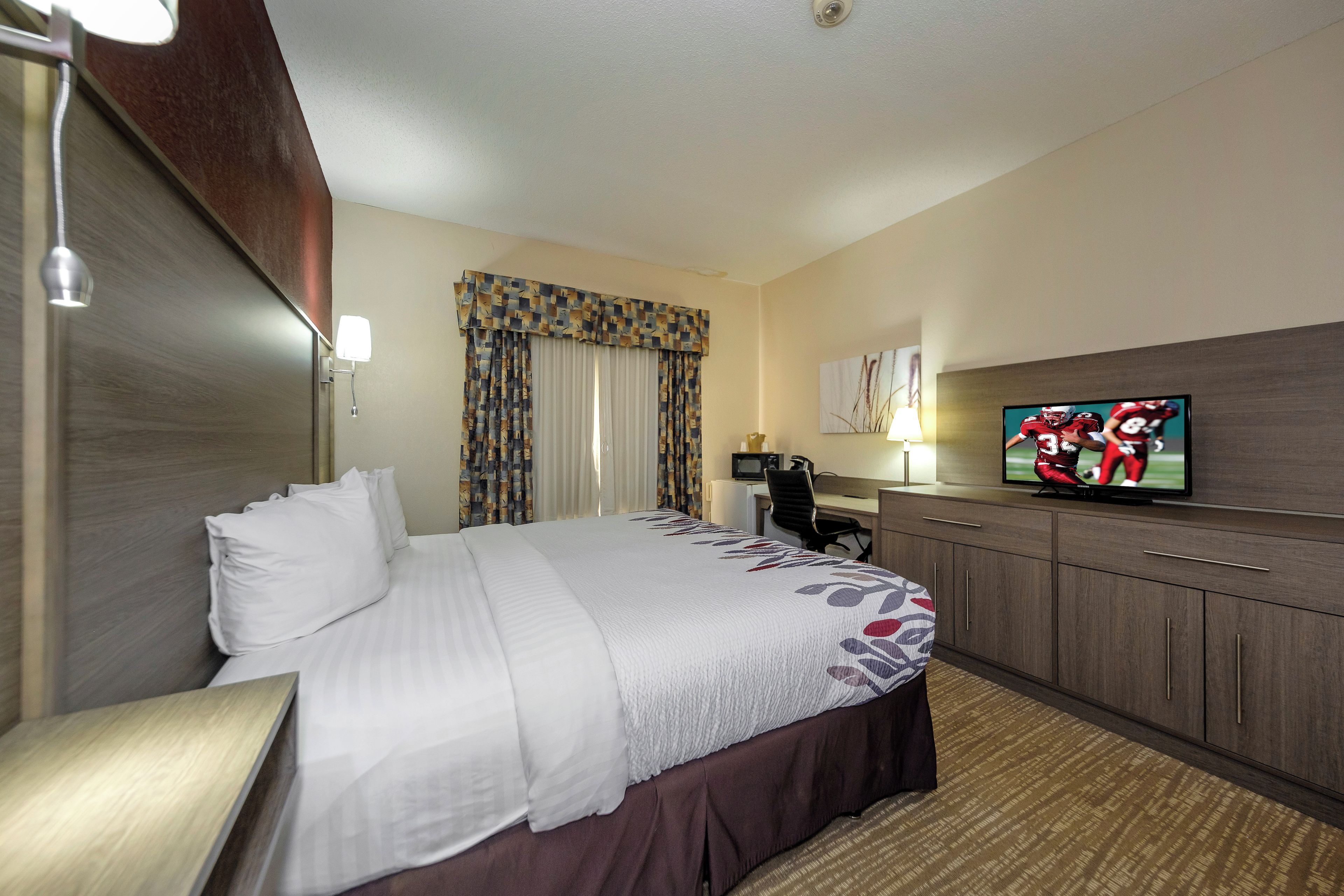 Ein Hotelzimmer mit Bett, Schreibtisch, Fernseher und Mikrowelle.