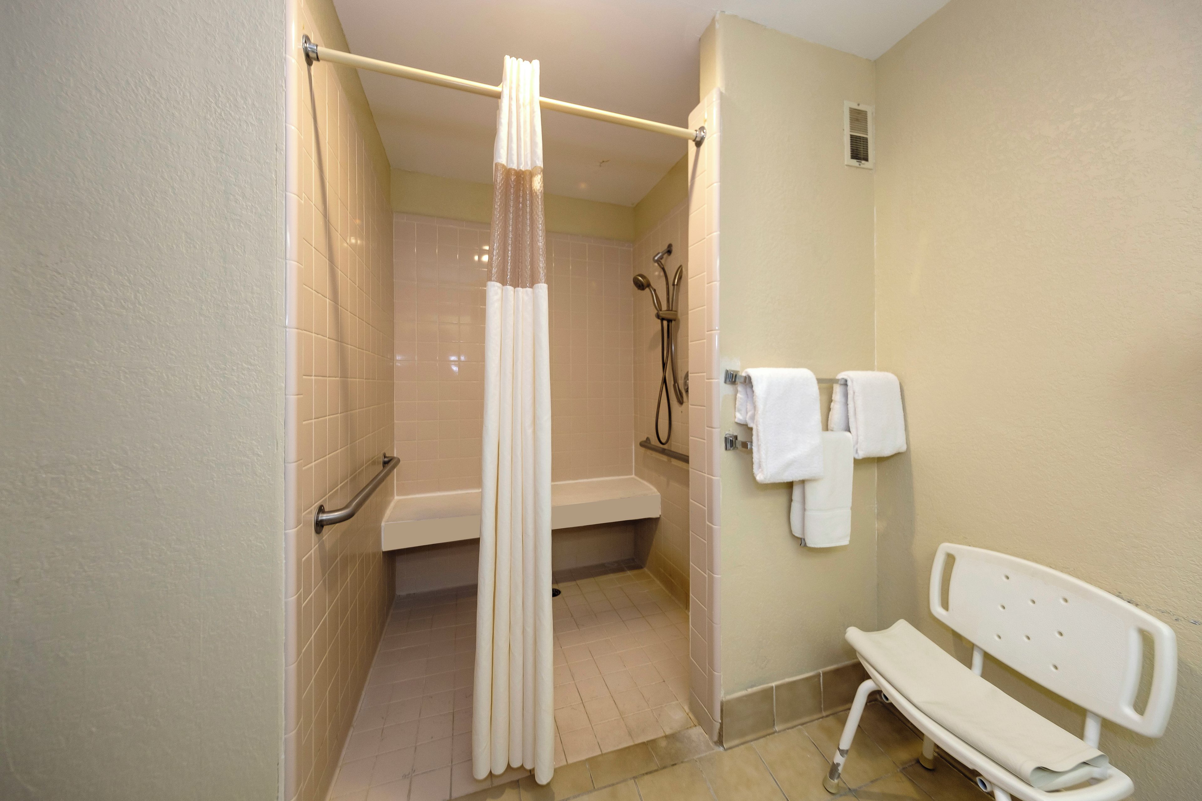 A bathroom with a shower, a bench, and a toilet.