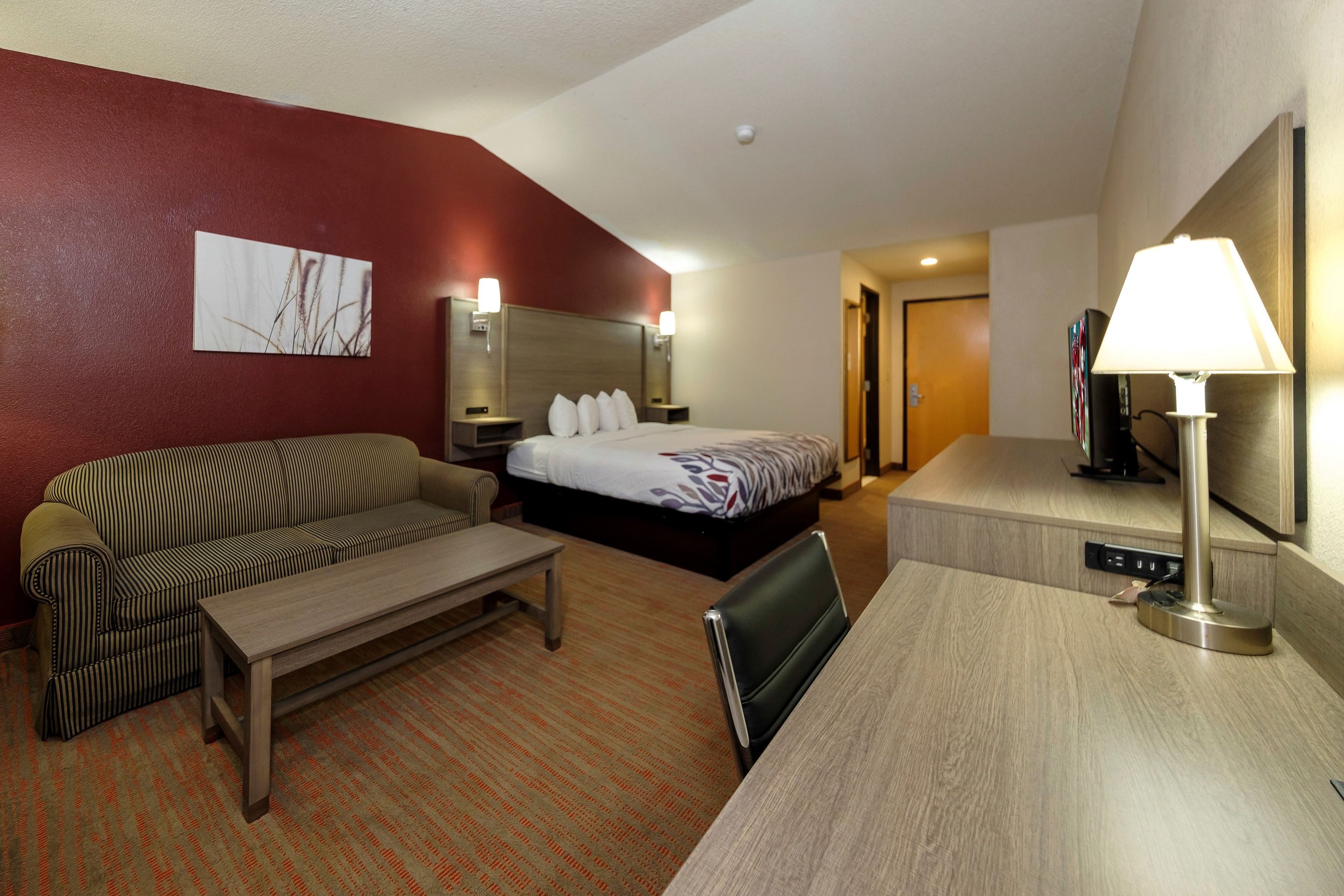 A hotel room with a bed, a sofa, a desk, and a lamp.