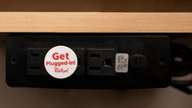 A power strip with a red plug-in label and a white label indicating voltage and frequency. - Red Roof Inn Yemassee (Yemassee)