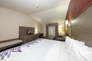 Una habitación de hotel con cama, escritorio, silla, televisión y ventana con cortinas.