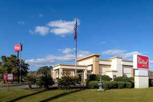 A Red Roof Inn & Suites building with a flagpole, a fountain, and well-maintained landscaping.