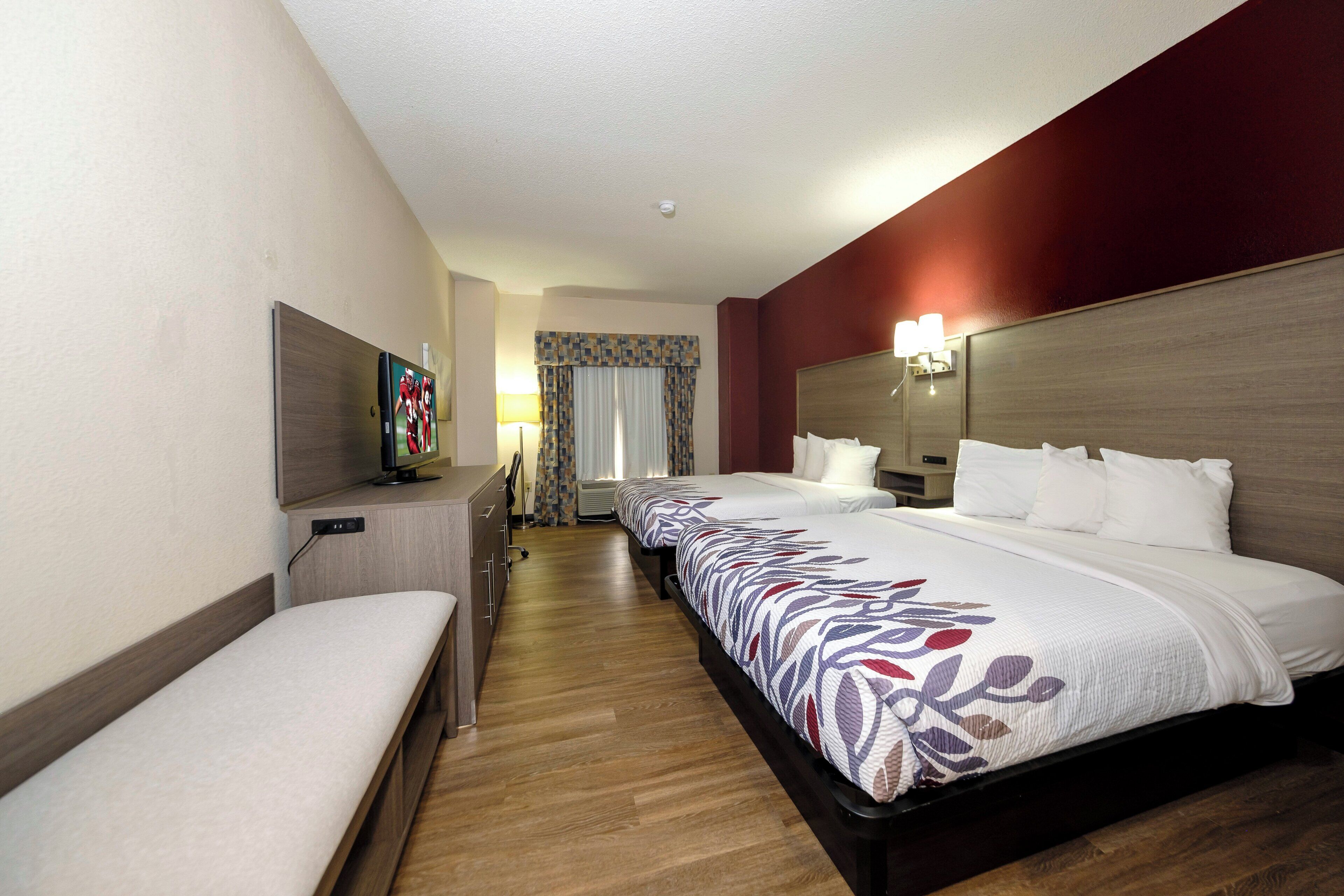 A hotel room with a bed, a desk, a TV, and a window with curtains.
