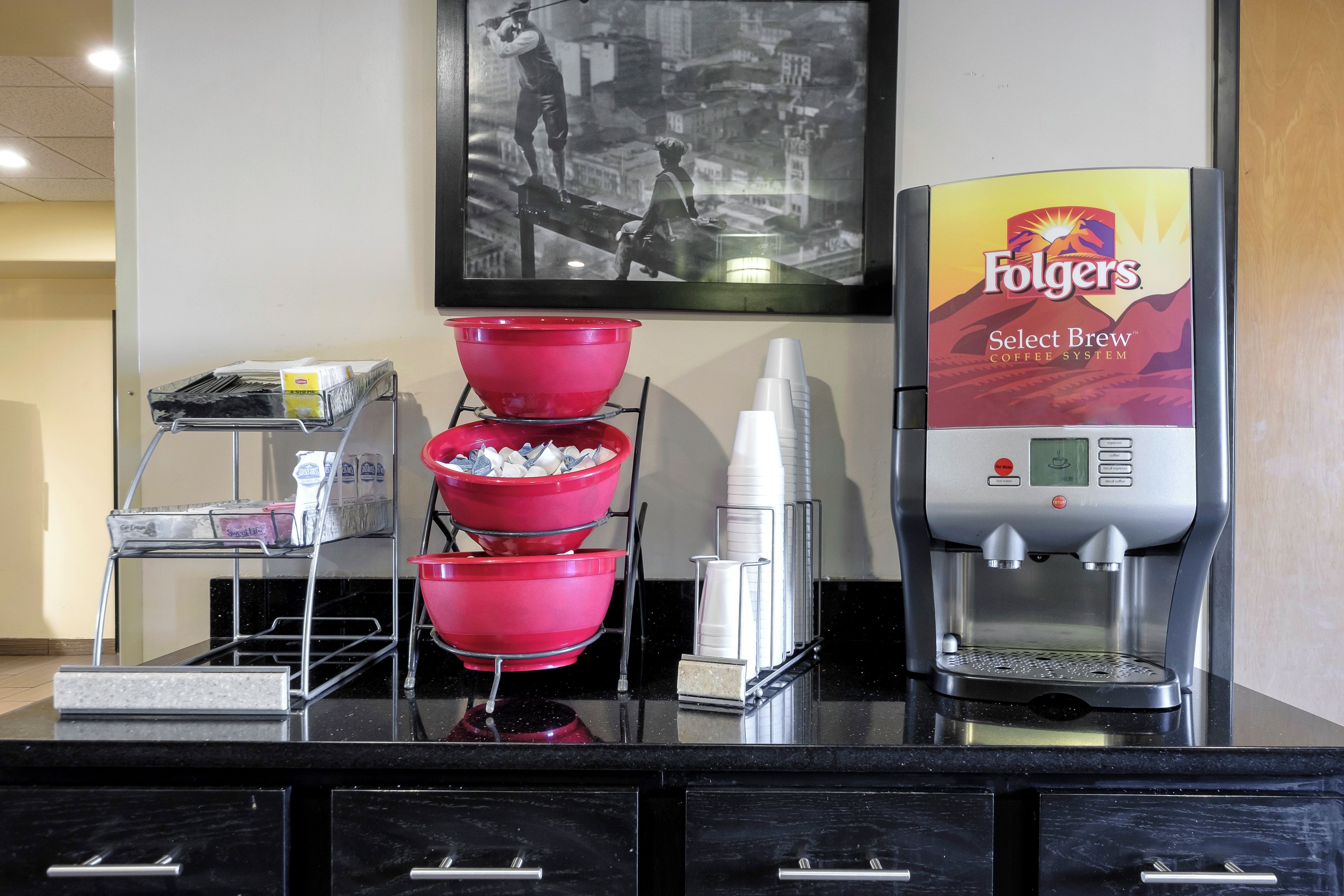 A coffee station with a Folgers coffee machine, red coffee dispensers, and a milk frother.