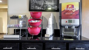 A coffee station with a Folgers coffee machine, red coffee dispensers, and a milk frother. - Red Roof Inn Yemassee (Yemassee)