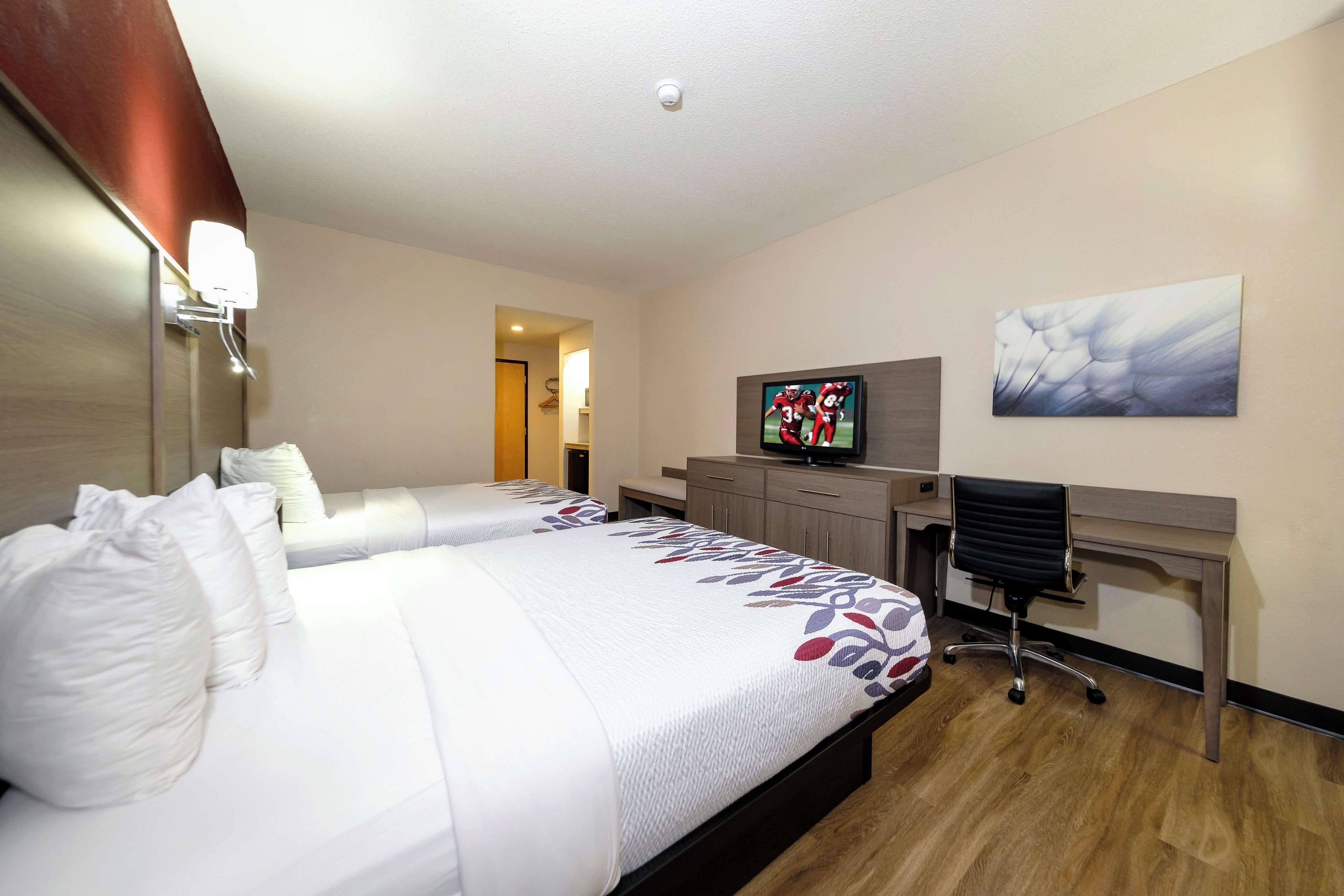 Habitación de hotel con dos camas, un escritorio, un televisor y un cuadro en la pared.