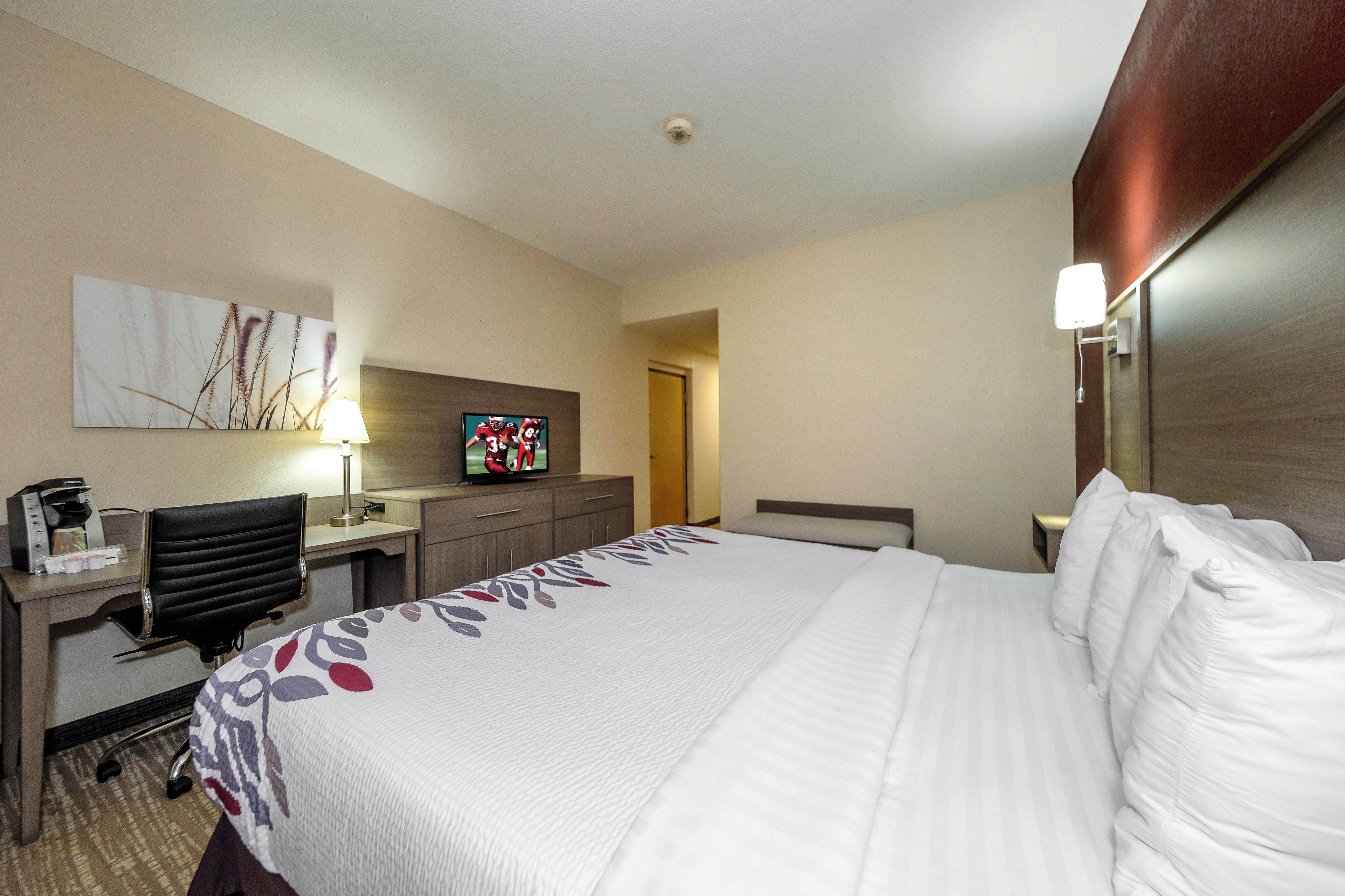 A hotel room with a bed, a desk with a chair, a television, and a coffee maker.