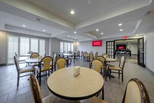 A hotel conference room with tables and chairs, a television screen displaying 'Free Wi-Fi All Rooms,' and an exit sign.