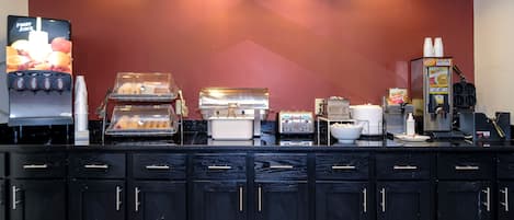 Una estación de desayuno autoservicio con una máquina de café, un tostador y un dispensador de bebidas.