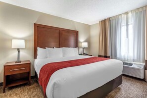 A hotel room with a large bed, two bedside tables with lamps, a red throw blanket, and a window with curtains.